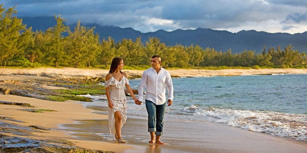Couple holding hands walking on the beach wearing white and denim
